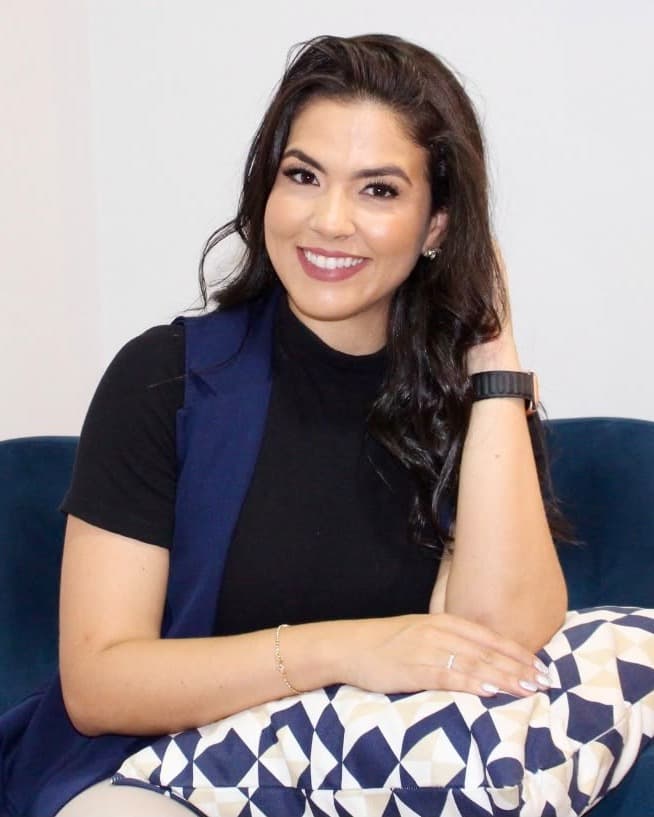 Stéfany Brito, psicóloga, sorrindo sentada em uma poltrona azul no consultório